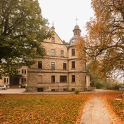 Schloss Hamborn im herbstlichen Licht, umgeben von leuchtenden Blättern und altem Baumbestand.