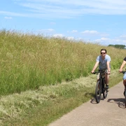 Radfahren in der Mittelweser-Region Zwei Personen, die auf einem asphaltierten Weg durch eine grüne, ländliche Landschaft radeln.
