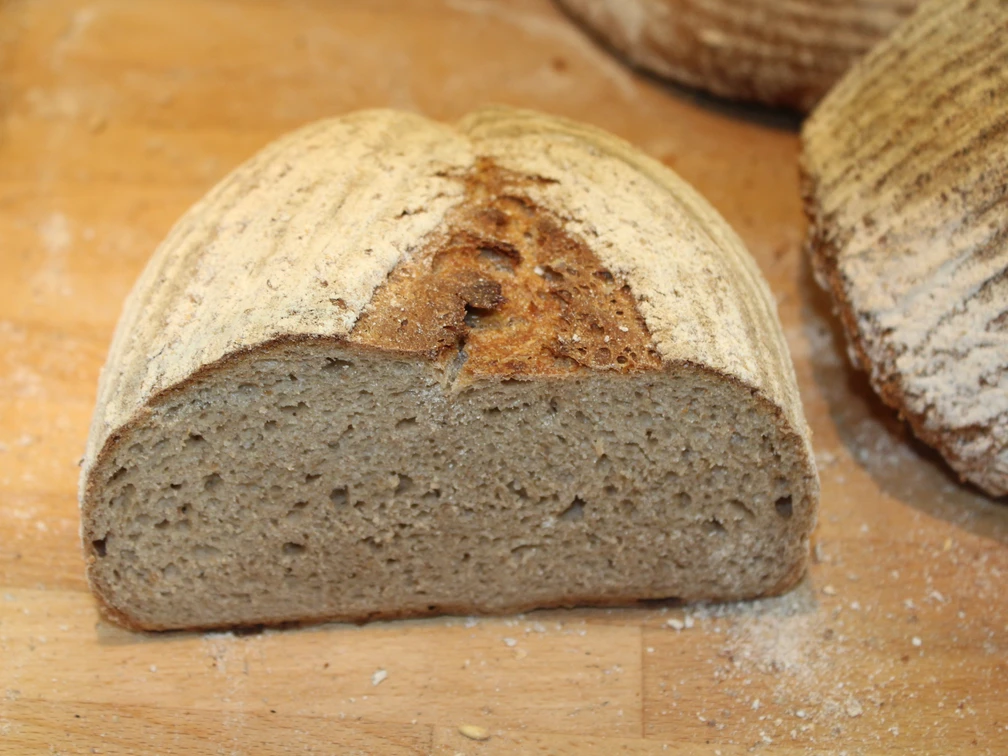 Brot Eine Scheibe körniges Vollkornbrot liegt auf einem Holzbrett, umgeben von Mehlkrümeln.