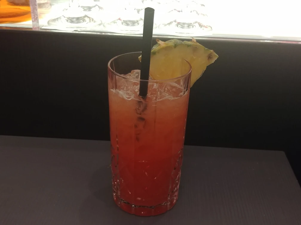 Cocktail Ein bunt geschichteter Cocktail in einem Kristallglas, dekoriert mit Ananasstück und schwarzem Strohhalm.