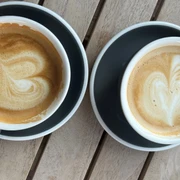 Kaffeetassen Zwei Kaffeetassen mit Latte Art in Herzform stehen auf grauen Tellern auf einem Holztisch.