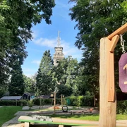 Minigolfplatz Waldkletterpark Velbert-Langenberg Ein Minigolfplatz mit Hindernis 13, umgeben von Bäumen, mit einem Turm im Hintergrund an einem sonnigen Tag.