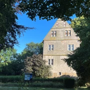 Burg Schlüsselburg Alte Burg mit steilem Dach aus hellem Stein, umgeben von Bäumen und einem blauen Himmel.