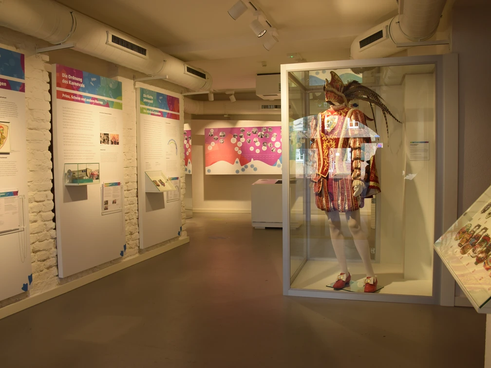 Karnevalskabinett in Monheim am Rhein Exponate im Karnevalsmuseum Monheim: bunte Schautafeln und ein prächtiges Kostüm in Vitrine.
