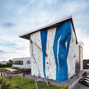 Bergstation Hilden Kletterhalle in modernem Design, großes Gebäude mit blauer und weißer Fassade, Parkplätze nahebei.