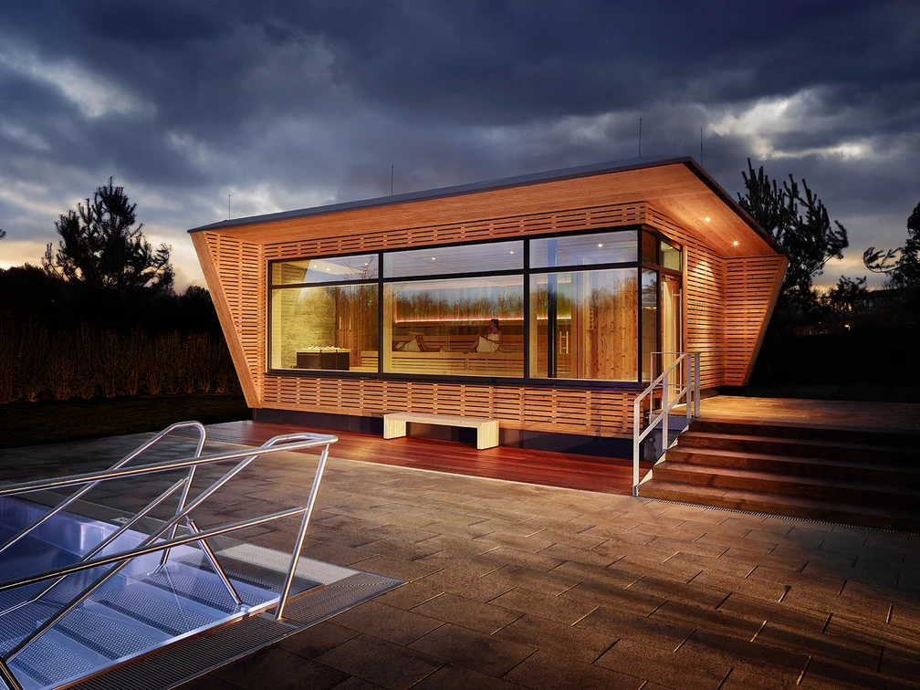 Mona Mare in Monheim am Rhein Modernes Gebäude mit großen Glasfronten, umgeben von beleuchteten Treppen und Gehwegplatten.