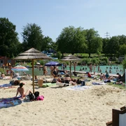 Naturfreibad Mettmann Ein Naturfreibad mit Sandstrand und Sonnenschirmen, umgeben von Bäumen und entspannenden Gästen.