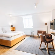 Helles, modernes Hotelzimmer mit Doppelbett, Schreibtisch, Stuhl und Wandfernseher in stilvollem Design.