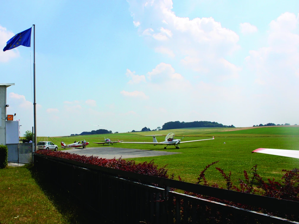 Segelflugplatz Meiersberg in Heiligenhaus Segelflugzeuge stehen auf einem weitläufigen, grünen Flugfeld unter einem blauen Himmel.