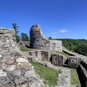Ruinen der Falkenburg mit erhaltenem Turmstumpf im Hintergrund, umgeben von grünen Wäldern.