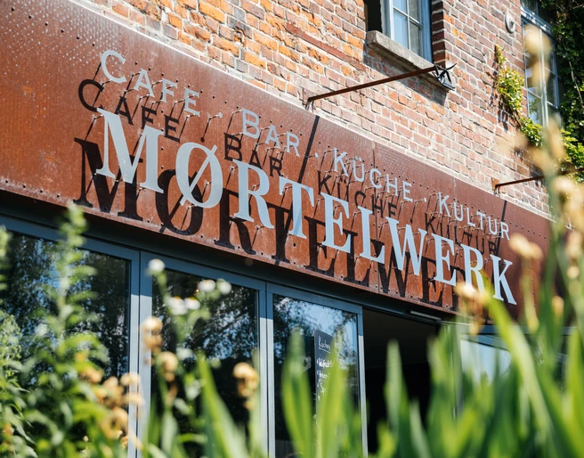 Moertelwerk - Gastronomie in Leipzig Blick auf die Backsteinfassade mit Schriftzug Moertelwerk, umrandet von Pflanzen, gastronomie, freisitz