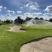 Golfclub Haan-Düsseltal Eine gepflegte Rasenfläche mit Sandbunkern, im Hintergrund ein Clubhaus und ein Wasserhindernis.
