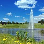 GC Velbert Ein gepflegter Golfplatz mit sauberem Gewässer und sprudelndem Springbrunnen unter blauem Himmel.
