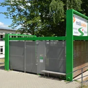 Mobilstation am Bahnhof Grüne Mobilstation am Bahnhof mit Fahrradständern und überdachten Sitzmöglichkeiten vor Bäumen.