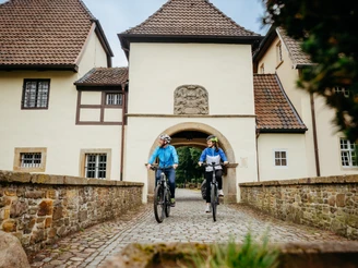 Radfahren auf der Artland-Rad-Tour Zwei Radfahrer passieren ein historisches Torhaus auf Kopfsteinpflaster.