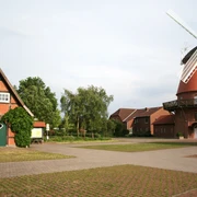Landesbergen Hochzeitsmühle Rote Backsteinmühle mit weißen Flügeln neben grünem Fachwerkhaus, umgeben von Bäumen und Weg.