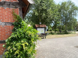 Mühlenplatz Landesbergen Backsteinhaus mit Efeu bewachsen, neben Sitzbänken und Infotafel auf einem gepflasterten Platz.