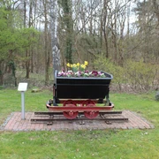 Sandlore Eine historische Lore auf Gleisen, die mit bunten Frühlingsblumen bepflanzt ist, steht im Grünen.
