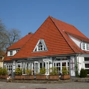 Alte Feuerwache Ein Gebäude mit rotem Ziegeldach und großen Fenstern, umgeben von grüner Vegetation und blauen Himmel.