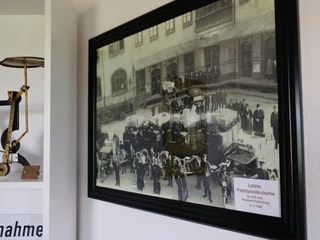Postmuseum Bokel Das Bild zeigt ein gerahmtes historisches Foto im Postmuseum Bokel, mit der Aufschrift „Letzte Paketpostkutsche“ und verschiedenen Exponaten im Vordergrund. Die Ausstellung vermittelt einen Eindruck von der Geschichte der Postzustellung.