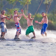 Wasserskianlage Langenfeld Vier junge Männer stehen auf Wakeboards, lachen und posieren fröhlich auf einer Wasserskianlage.