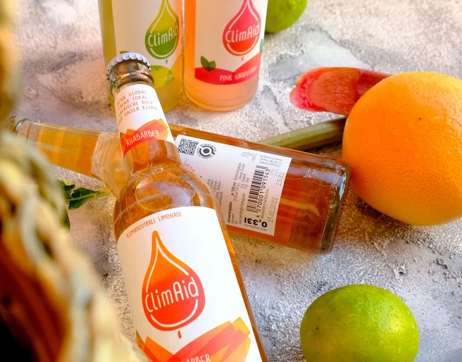 ClimAid Limonaden aus Haan ClimAid Limonadenflaschen liegen vor verschiedenen Zitrusfrüchten und versprechen erfrischenden Genuss.