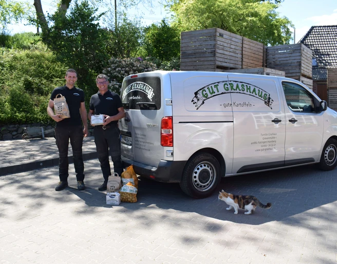 Gut Grashaus aus Ratingen Zwei Mitarbeitende stehen lächelnd neben einem Lieferwagen von Gut Grashaus, umgeben von Tierfutter.