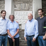 Familie Römer der Haaner Felsenquelle Eine Familie steht vor einem Steinmonument mit der Aufschrift "Felsenquelle 1903". Alle vier Personen lächeln in die Kamera und tragen lässige Kleidung. Im Hintergrund sind steinerne Strukturen und grünes Laub zu sehen.