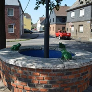 Kradepohl in Monheim am Rhein Ein runder Brunnen aus Ziegelsteinen mit Froschfiguren steht an einer Straßenkreuzung in Monheim am Rhein.