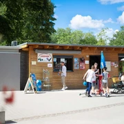 Tourist-Information Giebner in Monheim am Rhein Tourist-Information mit Holzverkleidung, Menschen und Fahrradführungen, umgeben von grünem Park.