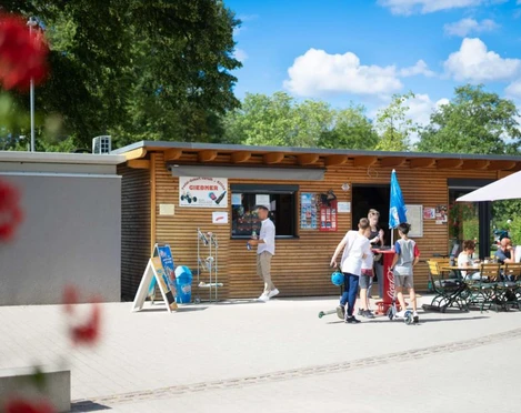 Tourist-Information Giebner in Monheim am Rhein Tourist-Information mit Holzverkleidung, Menschen und Fahrradführungen, umgeben von grünem Park.