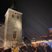 Weihnachtsmarkt2021_Platz Am Offers_StadtVelbert_Schuster_image00036.jpeg Menschen genießen den Weihnachtsmarkt rund um eine beleuchtete Kirche mit Turm im Abendlicht.