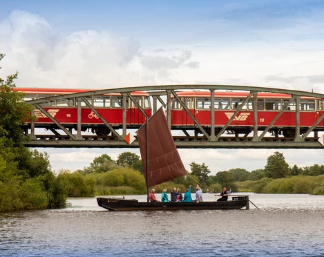 Mit dem Torfkahn auf der Hamme Ein Torfkahn fährt auf der Hamme vor der Eisenbahnbrücke, wo gerade der Moorexpress rüberfährt.