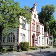 Rathaus von Erkrath Historisches Gebäude mit neugotischen Elementen, rotem Ziegelstein und Bäumen im Hintergrund.