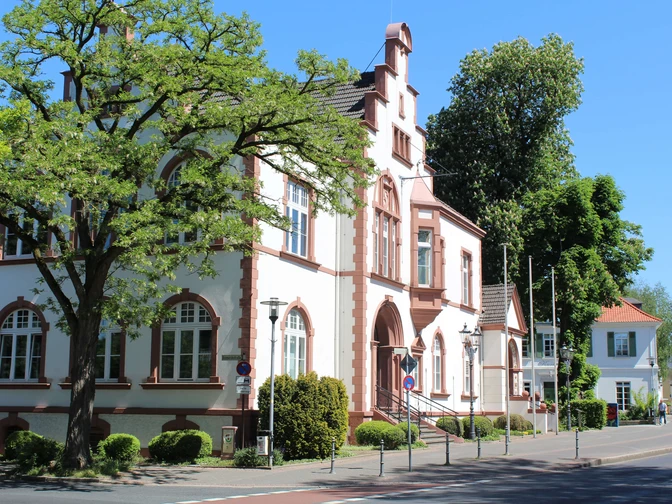 Rathaus von Erkrath Historisches Gebäude mit neugotischen Elementen, rotem Ziegelstein und Bäumen im Hintergrund.