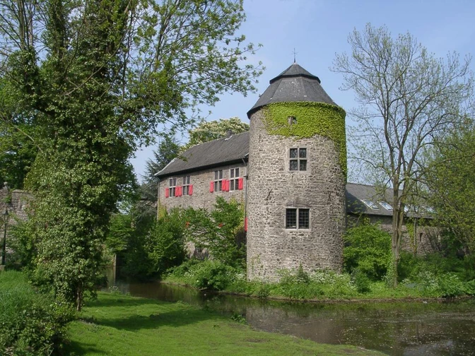 Wasserburg Haus zum Haus in Ratingen Wasserburg inmitten grüner Landschaft, umgeben von Wassergraben und bewachsenen Mauern aus Naturstein.