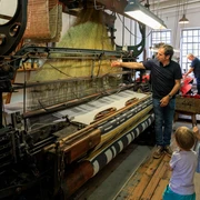Führung an laufenden Maschinen Historische Webmaschine mit Besuchergruppe, darunter Erwachsene und Kinder, in einem Museum.