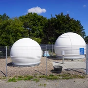 Volkssternwarte Langwedel Zwei weiße Kuppeln einer Sternwarte hinter einem Drahtzaun unter einem klaren blauen Himmel.