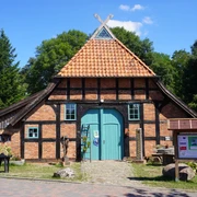 Häuslingshaus Langwedel Backsteinfachwerkhaus mit dunklen Holzbalken und rotem Ziegeldach neben Infotafel und Bäumen.