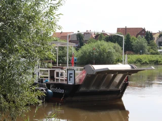 PetraSolara Ein Flussboot mit dem Namen PetraSolara liegt am Ufer, umgeben von üppigem Grün und Häusern.