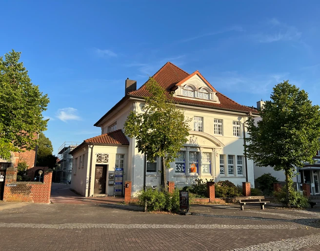Escape Room Ein großes, weißes Gebäude mit rotem Dach und Escape Room-Schildern an der Fassade, umgeben von Bäumen.