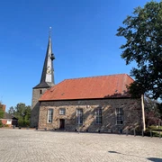 Rehburger Kirche mit markantem Turm, umgeben von Kopfsteinpflaster, sonniger blauer Himmel im Hintergrund.