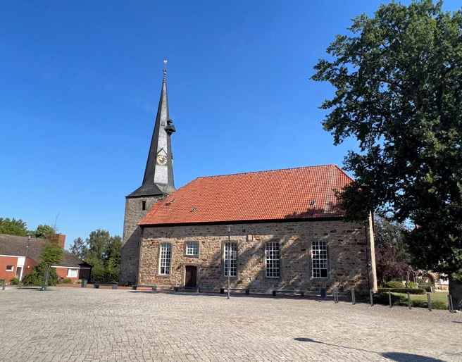 Rehburger Kirche mit markantem Turm, umgeben von Kopfsteinpflaster, sonniger blauer Himmel im Hintergrund.