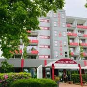 Hotel IM PARK, Bad Iburg Hotel IM PARK in Bad Iburg, modernes mehrstöckiges Gebäude mit rot-weißen Balkonen und grünem Umfeld.