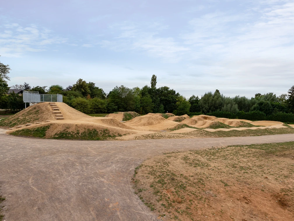 Dirt-Bike-Anlage Fernholz, Ratingen Weitläufige Dirt-Bike-Strecke mit Erdhügeln und Kurven, umgeben von Bäumen und freiem Himmel.