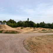 Dirt-Bike-Anlage Fernholz, Ratingen Weitläufige Dirt-Bike-Strecke mit Erdhügeln und Kurven, umgeben von Bäumen und freiem Himmel.
