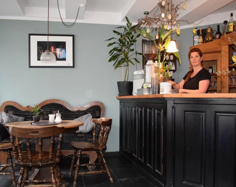 Café am Markt in Mettmann Einladendes Café mit Holzmöbeln, Bar, Wanddekoration und blühenden Pflanzen im Inneren.