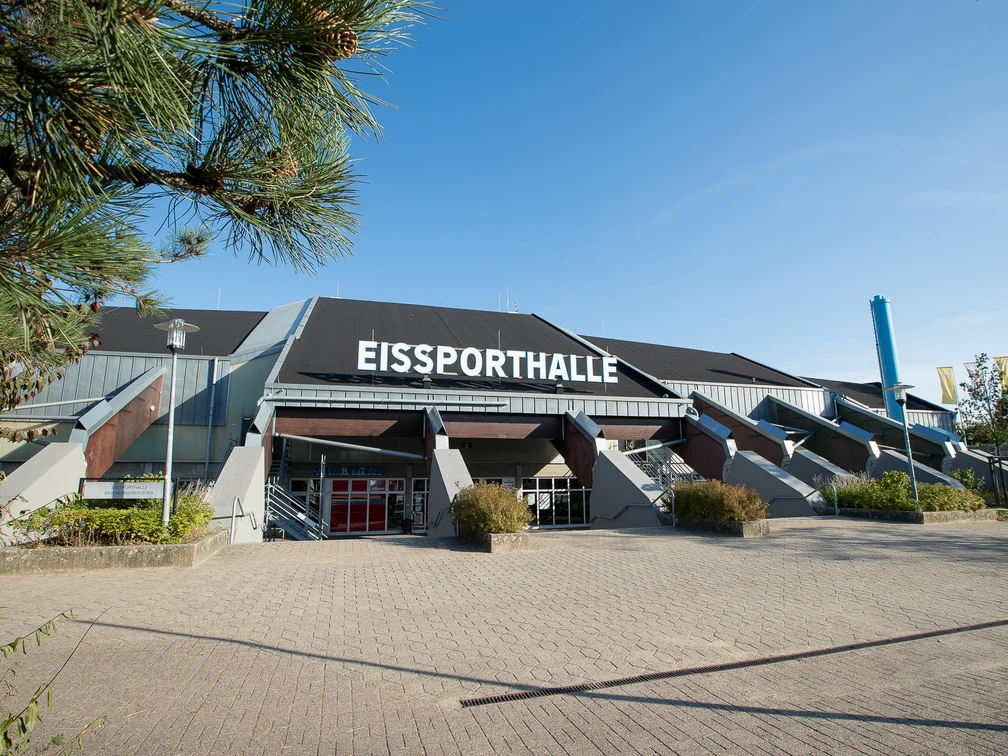 Eissporthalle Ratingen Große Eissporthalle in Ratingen mit markantem Dach, umgeben von Pflanzen und einem gepflasterten Vorplatz.