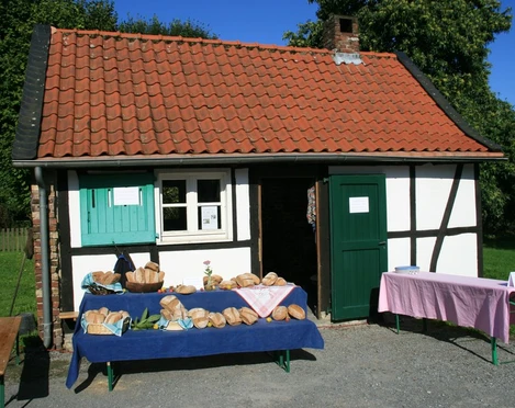 Brot backen im Historischen Backhaus in Erkrath Traditionelles Fachwerkgebäude mit Ziegeldach, Brote auf blauen Tischflächen im Freien vor dem Haus.