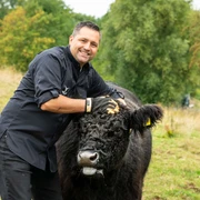 Dirk Hanten und Galloway-Rind Dirk Hanten streichelt ein Galloway-Rind auf einer grünen Wiese, im Hintergrund sind Bäume.